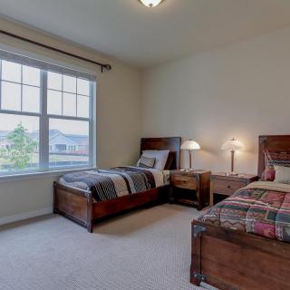 A cozy bedroom with twin beds, featuring wooden furniture and large windows.