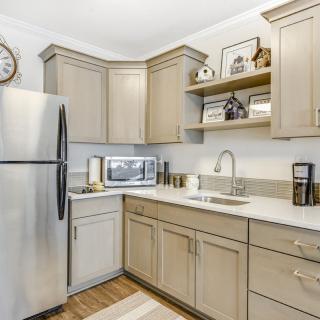 A modern kitchen featuring a stainless steel refrigerator, microwave, and beige cabinets with open shelving.