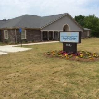 A church building with a sign in front, surrounded by grass and flowers.