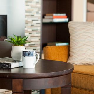 A cozy living room setup with a coffee table, books, a plant, and a mug beside a comfortable sofa.
