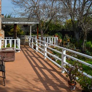 A sunny outdoor deck overlooking a garden, surrounded by a white fence and featuring patio furniture.