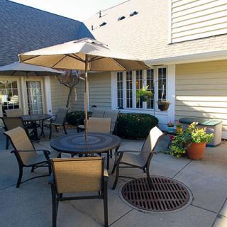 A sunny patio with a table, chairs, and an umbrella, surrounded by potted plants.
