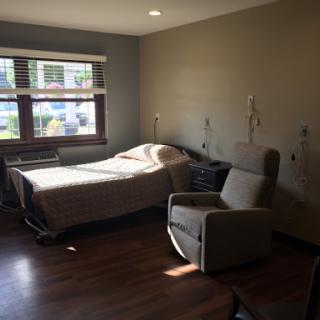 A well-lit patient room in a hospital, featuring a bed and a chair by the window.