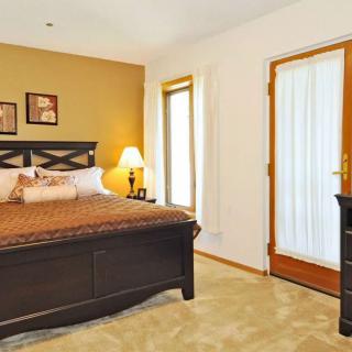 A cozy bedroom with a comfortable bed, warm lighting from a lamp, and natural light streaming through the windows.