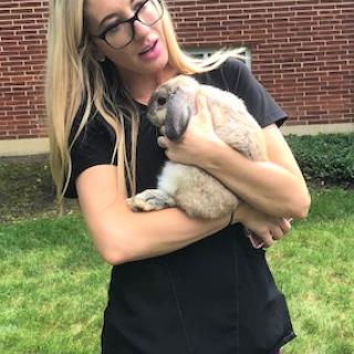 A woman gently holds a rabbit while enjoying a sunny day outdoors.