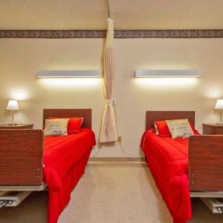 A hospital room with two twin beds featuring red bedding and warm lighting.