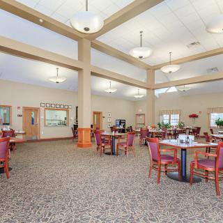A spacious dining room with multiple tables and chairs, well-lit by ceiling lights.