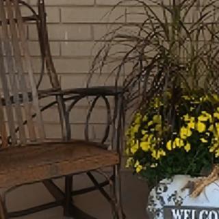 A cozy porch with a rocking chair, potted flowers, and a welcome sign.