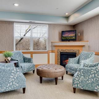 A cozy living room with patterned armchairs, a central coffee table, and a fireplace beneath a wall-mounted television.