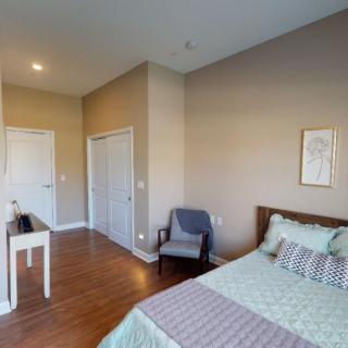 A cozy bedroom with a neatly made bed, wooden flooring, a chair, and minimalistic wall decor.