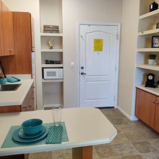 A modern kitchen with a dining area, featuring wooden cabinets, an open shelf concept, and teal-colored dishware.