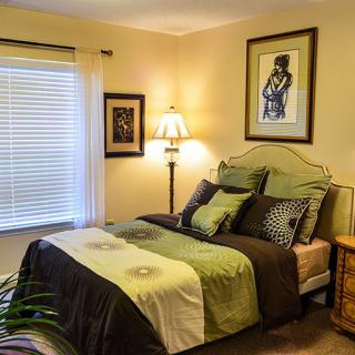 A cozy bedroom with a neatly made bed, decorative pillows, and framed artwork on the walls.