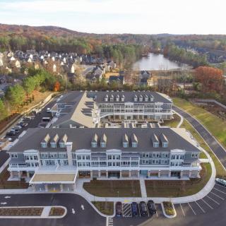 Aerial view of a commercial building complex with a parking lot, surrounded by trees and a lake.