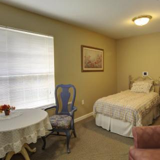 A cozy bedroom with a single bed, a small table, and a window with blinds.
