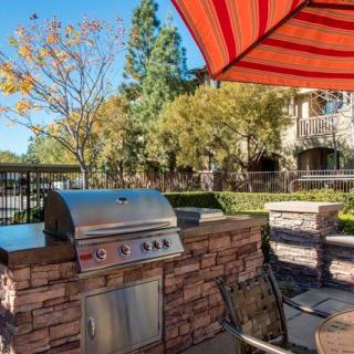 An outdoor patio with a barbecue grill and seating area under a red-striped umbrella.