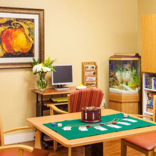 A cozy office space with a desk, computer, and artwork on the wall. There are chairs surrounding a table, an aquarium in the corner, and a bookshelf nearby.
