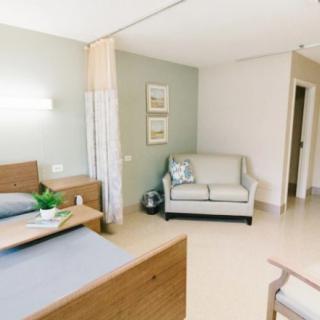 A modern hospital room featuring two beds and a small seating area.