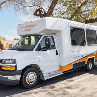 A white shuttle van parked under a tree, featuring an orange accent.