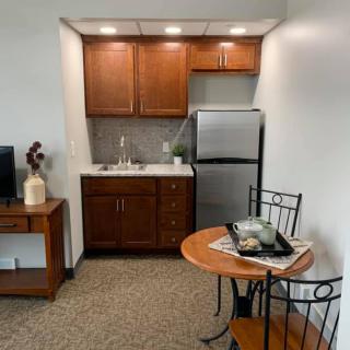 A compact kitchenette with wooden cabinets, a small fridge, and a cozy dining setup featuring a round table with chairs.