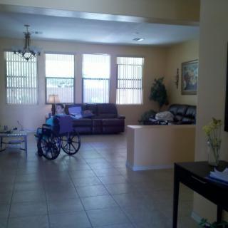 A spacious living room with a sofa, wheelchair, and large windows.