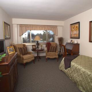 A cozy bedroom with two chairs, a bed, and a large window.