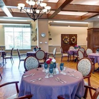 An elegantly set dining room with multiple tables and chairs, featuring a chandelier and soft lighting.