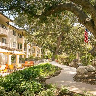 A serene garden path lined with trees and outdoor seating adjacent to a building, featuring an American flag.