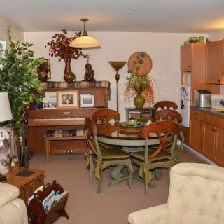 A cozy living room with a dining area featuring a piano and decorative plants.