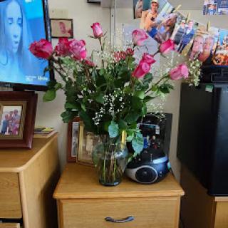A vibrant bouquet of pink roses displayed in a vase next to a television and framed photographs.