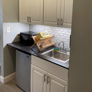 A small kitchen area with a sink, dish rack, and cabinets.