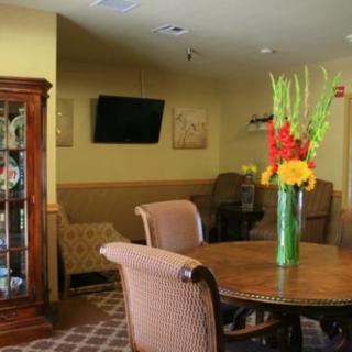 A cozy lounge area featuring a wooden table with chairs, a vibrant floral arrangement, and a wall-mounted television.