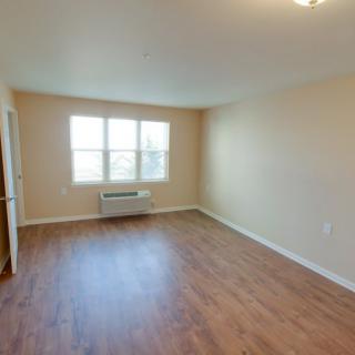 A vacant room with wooden flooring and ample natural light from a large window.