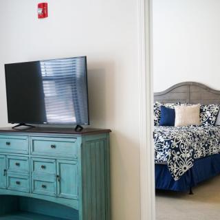 A cozy bedroom with a TV on a teal dresser and patterned bedding in the background.