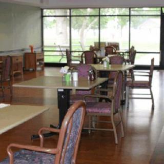 An empty dining area with tables and chairs, featuring large windows in the background.
