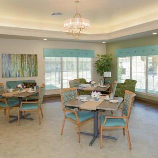 A bright and elegantly designed dining room with multiple tables and chairs, featuring large windows and a chandelier.