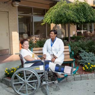A doctor conversing with a patient in a wheelchair outside a medical facility.