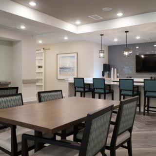 A modern dining area with a large table, chairs, and a kitchen bar with overhead lighting.