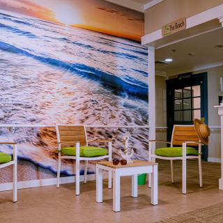 A cozy waiting area featuring green-cushioned chairs and a vibrant beach mural.
