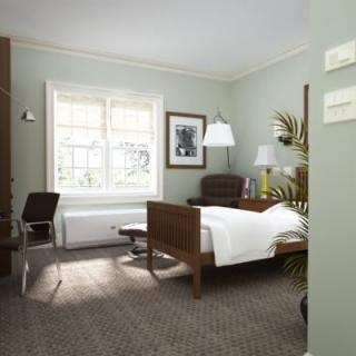 A cozy bedroom with a wooden bed, armchair, and desk next to a large window.