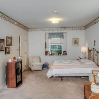 A cozy bedroom with a bed, chair, and various decor elements such as framed pictures and a lamp.