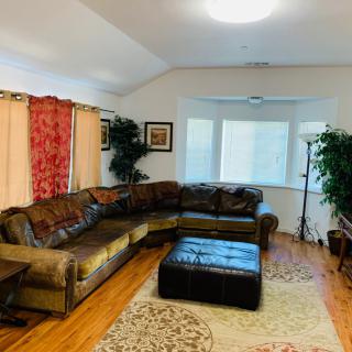 A cozy living room with a leather sectional sofa, hardwood floors, and indoor plants.