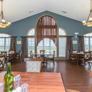 A spacious dining area featuring elegant chandeliers, multiple tables with chairs, large arched windows, and wood flooring.