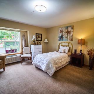 A cozy bedroom featuring a single bed with decorative pillows, surrounded by warm lighting and tasteful art on the walls.