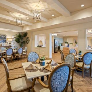 An elegantly decorated dining room with blue upholstered chairs and neatly set tables, featuring warm lighting and sophisticated decor.