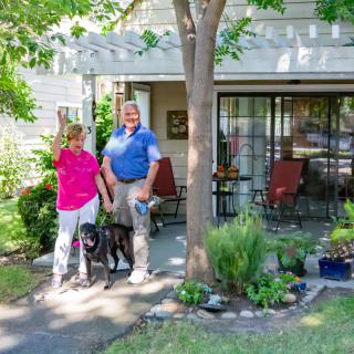 A couple standing with their dog in front of their house with a garden and porch.