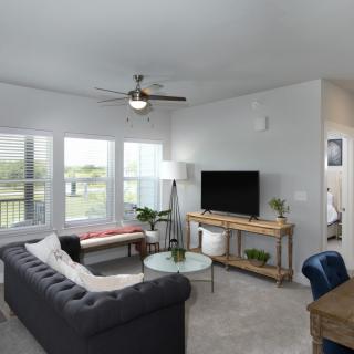 A modern living room with a large sofa, television, and ample natural light from multiple windows.