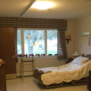 A tidy hospital room featuring a single bed, window with curtains, and basic furnishings.