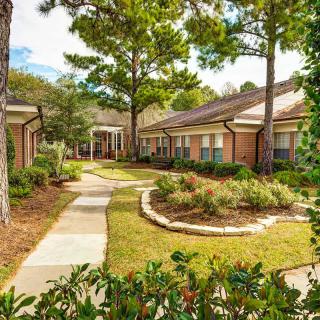 A serene garden pathway surrounded by greenery and trees, leading to a brick building.