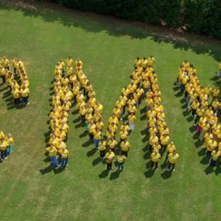 A group of people in yellow shirts form the letters 'CMU' on a grassy field.