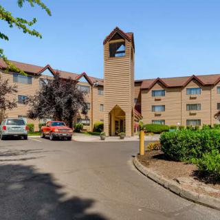 A hotel building with a parking lot and cars in front, surrounded by trees.